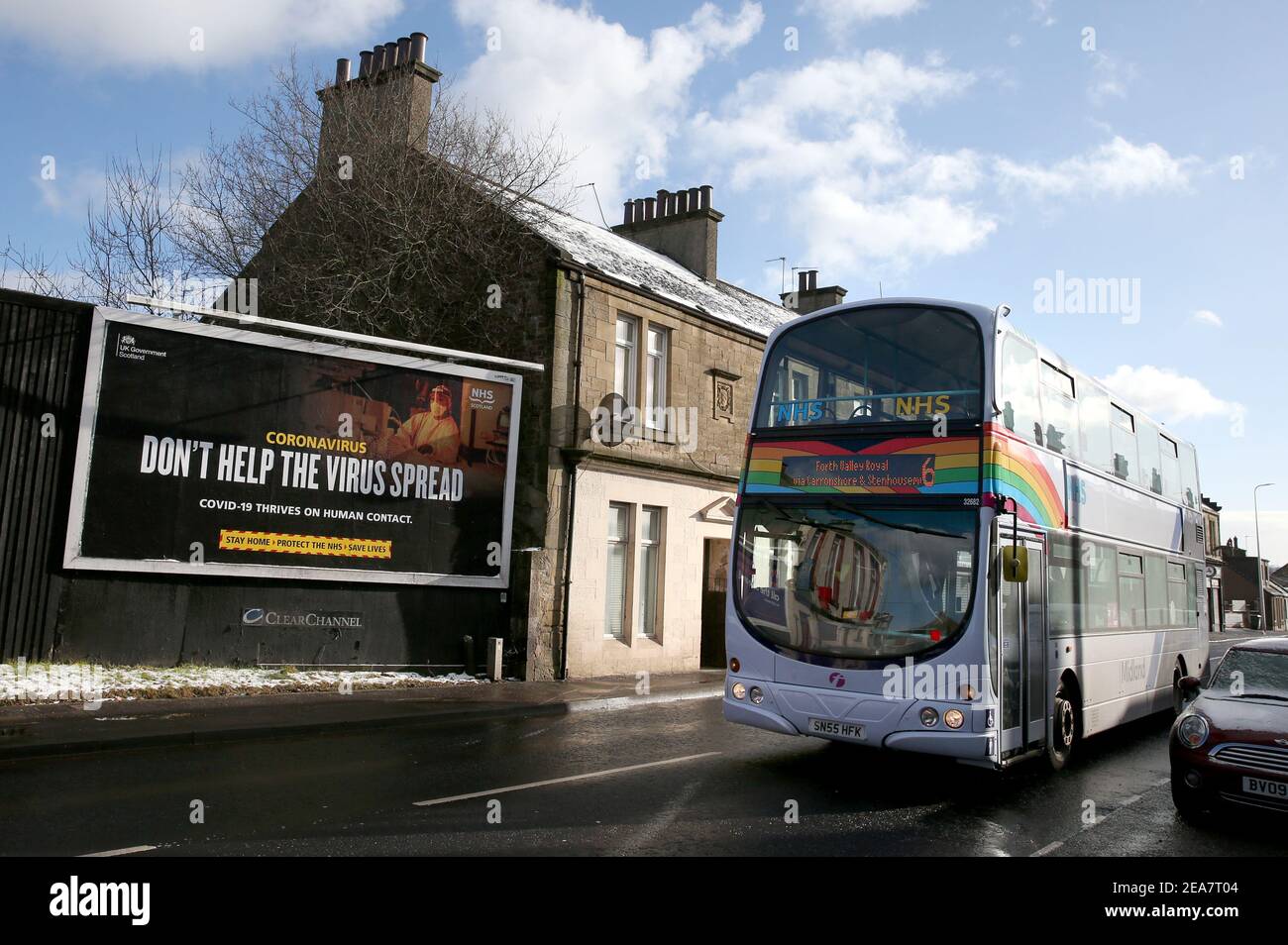 Ein Bus, der mit Regenbogen und NHS-Aufklebern geschmückt ist, fährt an einer Werbeplakette im Zusammenhang mit Coronavirus in Falkirk, Zentralschottland, vorbei, wo die am 5. Januar für das schottische Festland eingeführten Lockdown-Maßnahmen bis mindestens Ende Februar in Kraft bleiben. Bilddatum: Montag, 8. Februar 2021. Stockfoto