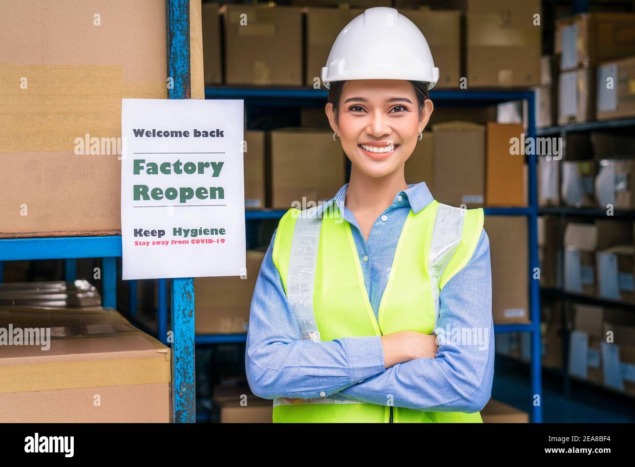 Portrait einer asiatischen Arbeiterin mit Sicherheitskleidung und Fabrik Öffnen Sie das Hinweisblatt erneut, und begrüßen Sie den Kunden wieder vor Ort Lager nach Covid Stockfoto