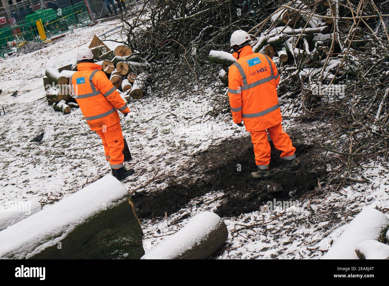 London, Großbritannien. Am dreizehnten Tag der Räumungen auf dem Euston Square graben HS2 Arbeiter am Euston Square, London, Großbritannien, weiter im Schnee. Februar 2021, 8th. Baumstämme und Äste von den gefällten Platanen liegen verstreut herum. Das Anti-HS2-Lager wird weiterhin von Gerichtsvollzieher (vom National Enforcement Team, NET, einer Tochtergesellschaft der High Court Enforcement Group) am Bahnhof Euston geräumt (um einen temporären Parkplatz zu schaffen). Alle oben genannten Demonstranten wurden geräumt und beginnen nun, um die Tunnel herum zu graben.: Denise Laura Baker/Alamy Live News Stockfoto