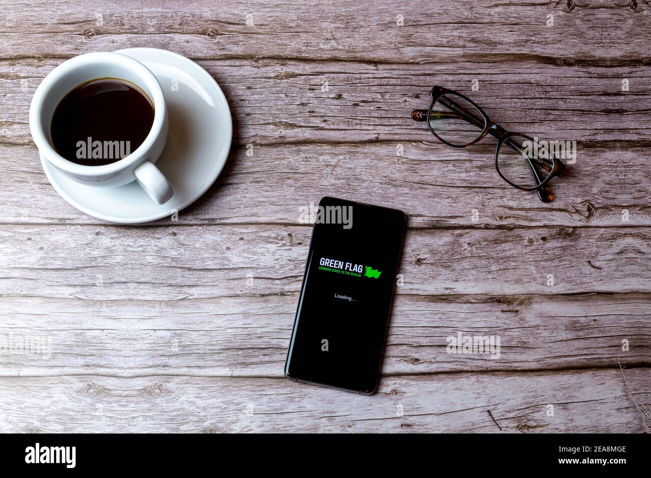 Ein Handy oder Handy auf einem Holz gelegt Tabelle mit der Green Flag Auto Pannenhilfe App öffnen weiter Zu einem Kaffee Stockfoto