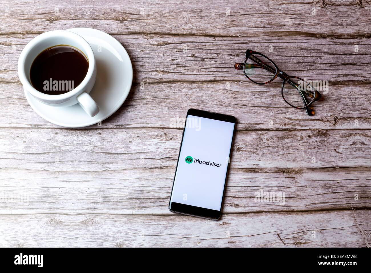 Ein Handy oder Handy auf einem Holz gelegt Tabelle mit der Tripadvisor Reisebericht App geöffnet neben Ein Kaffee Stockfoto