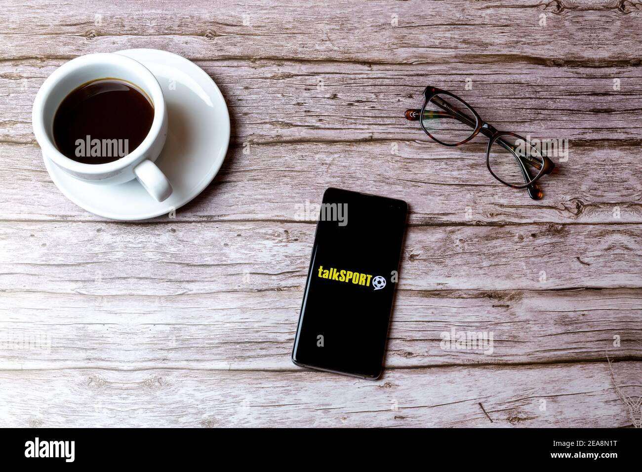Ein Handy oder Handy auf einem Holz gelegt Tabelle mit der Talk Sport Radio App geöffnet neben Ein Kaffee Stockfoto
