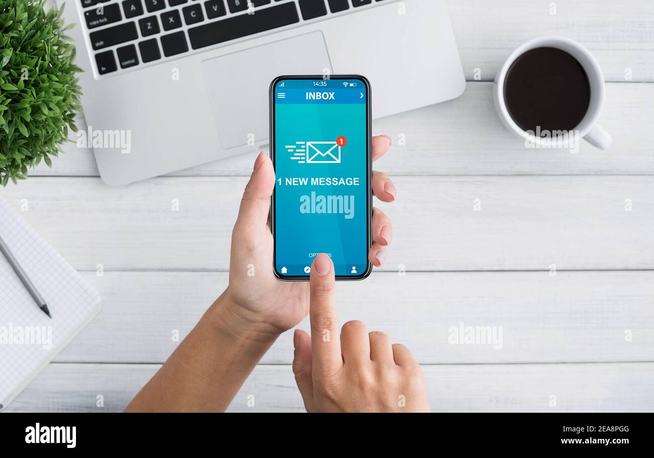 Frau hält Smartphone mit neuer E-Mail-Nachricht am Arbeitsplatz Stockfoto