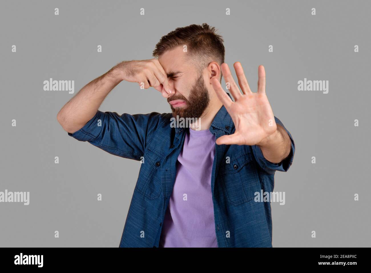 Schrecklicher Geruch. Millennial Hipster Kerl schließt seine Nase und gestikulieren STOPPEN, Gefühl angewidert auf grauen Studio-Hintergrund Stockfoto