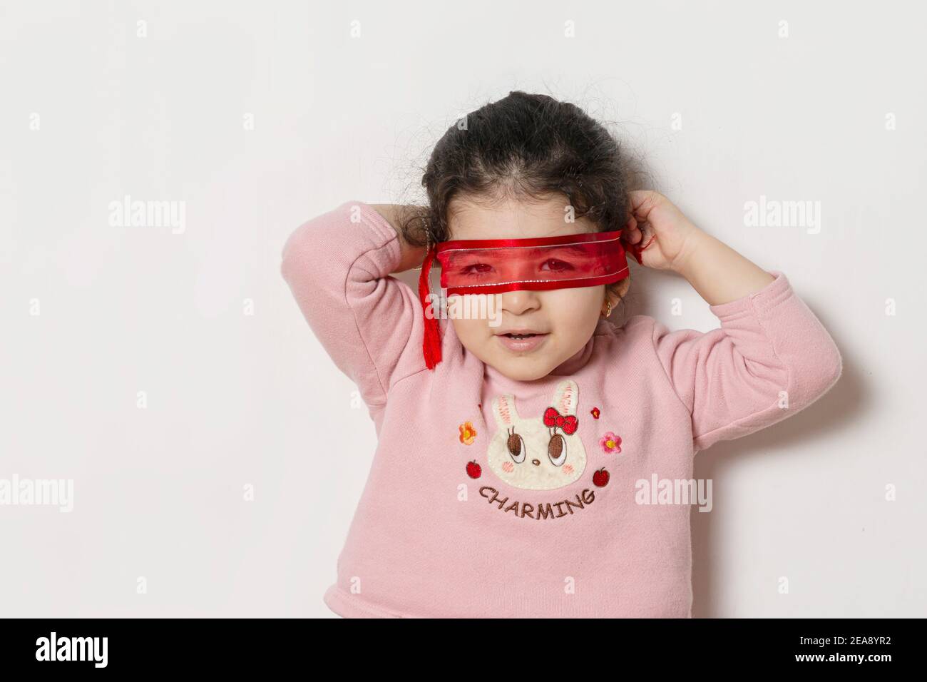 Kleines Mädchen bedeckte ihre Augen mit einem roten Band, Superhelden Konzept Stockfoto