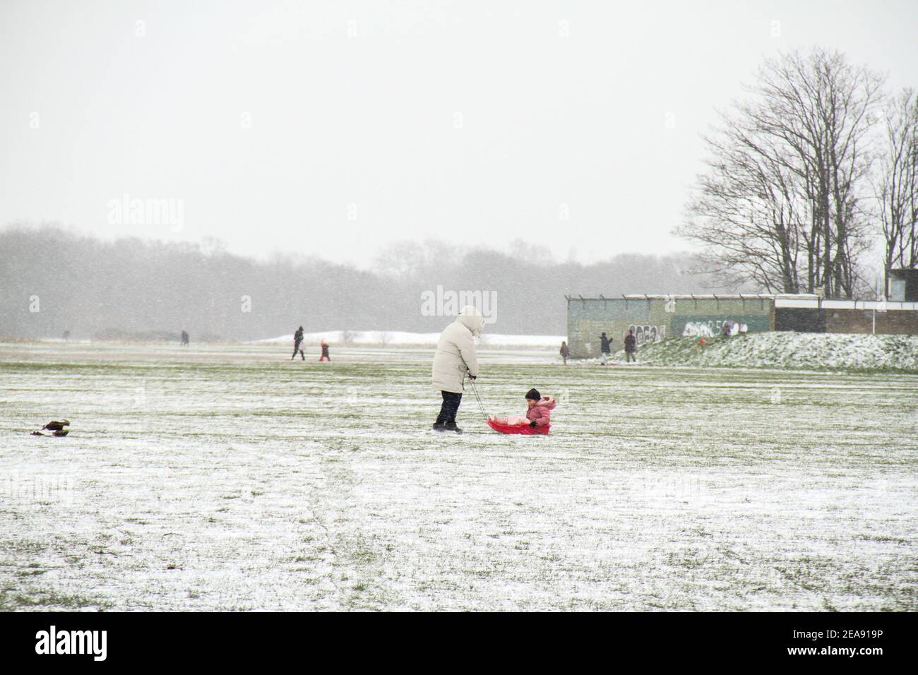 Ein Mann sah, wie er mit einem Kind einen Schlitten auf einem schneebedeckten Teil des Wansted Park zog. Schwerer Schnee und Eis haben Teile des Vereinigten Königreichs gestört, und London erhielt etwa 5cm Schnee. Die starken Ostwinde des Sturms Darcy haben die Temperaturen in Teilen Großbritanniens auf unter minus eins gesunken. Stockfoto