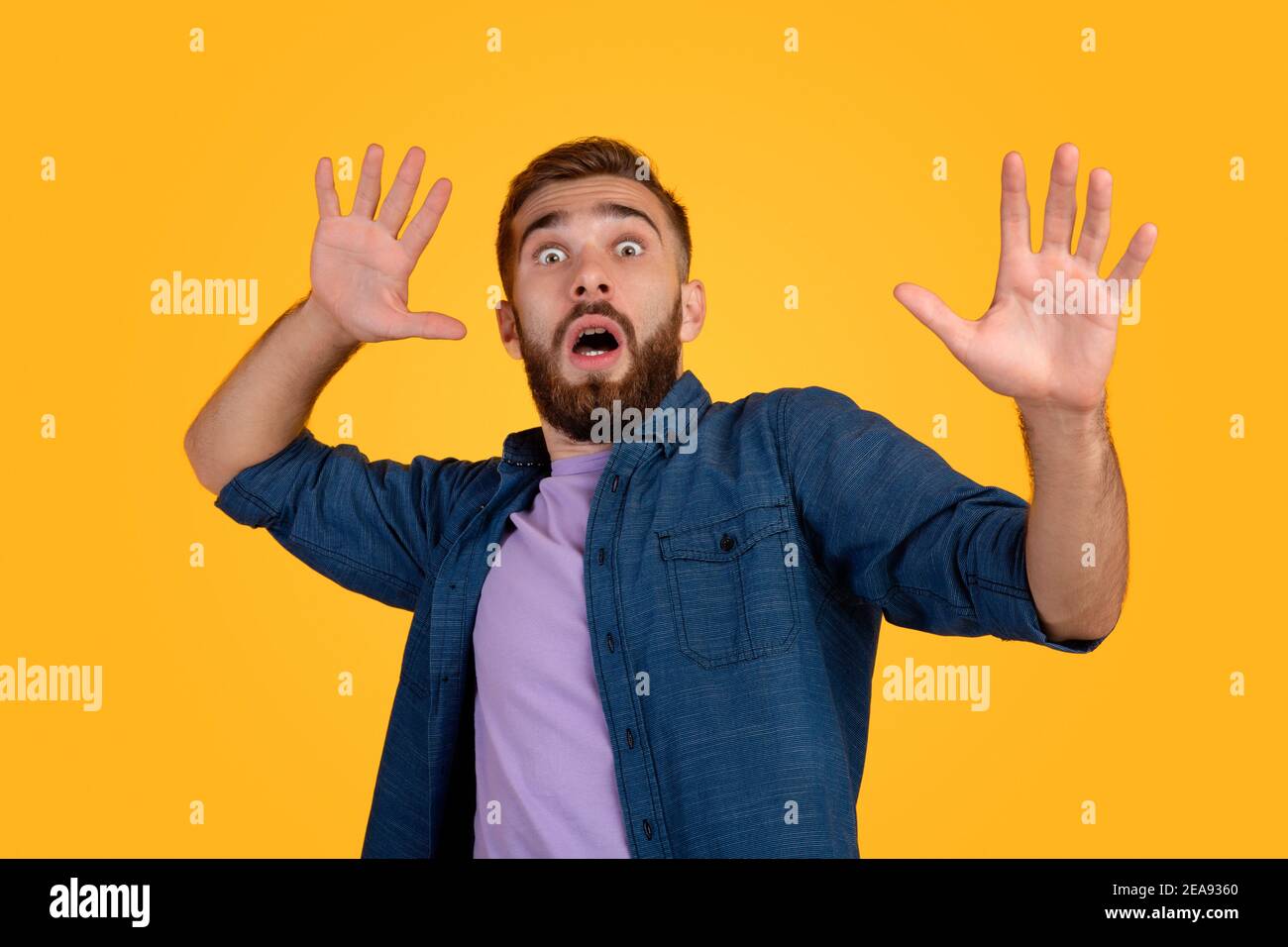 Ängstlicher kaukasischer Mann macht verängstigte Geste mit seinen Händen, versucht, sich auf orangenen Studio Hintergrund zu verteidigen Stockfoto