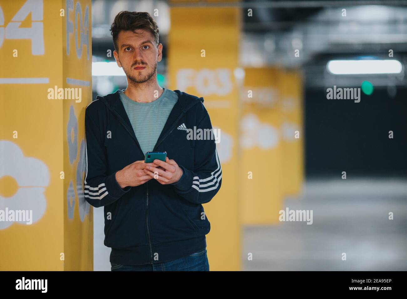 BANJA LUKA, BOSNIEN UND HERZEGOWINA - Nov 27, 2019: Mann trägt Adidas- Trainingsanzug in der Garage hält Telefon Stockfotografie - Alamy