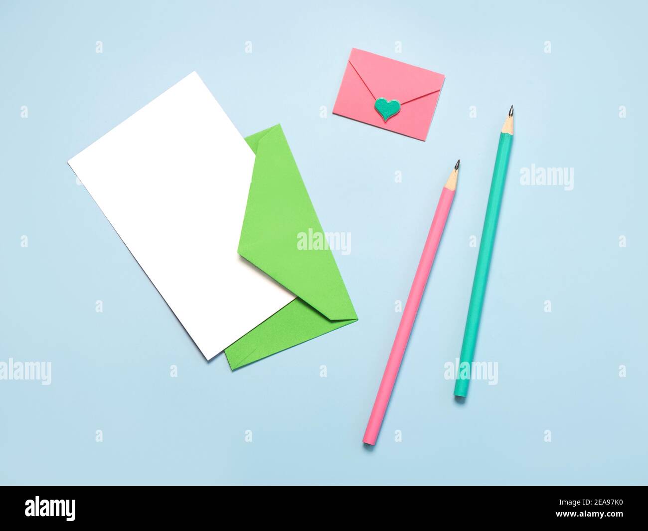 Grüner Papierumschlag mit weißer Karte, pinker Papierumschlag pink und grüne Stifte auf blauem Hintergrund Stockfoto