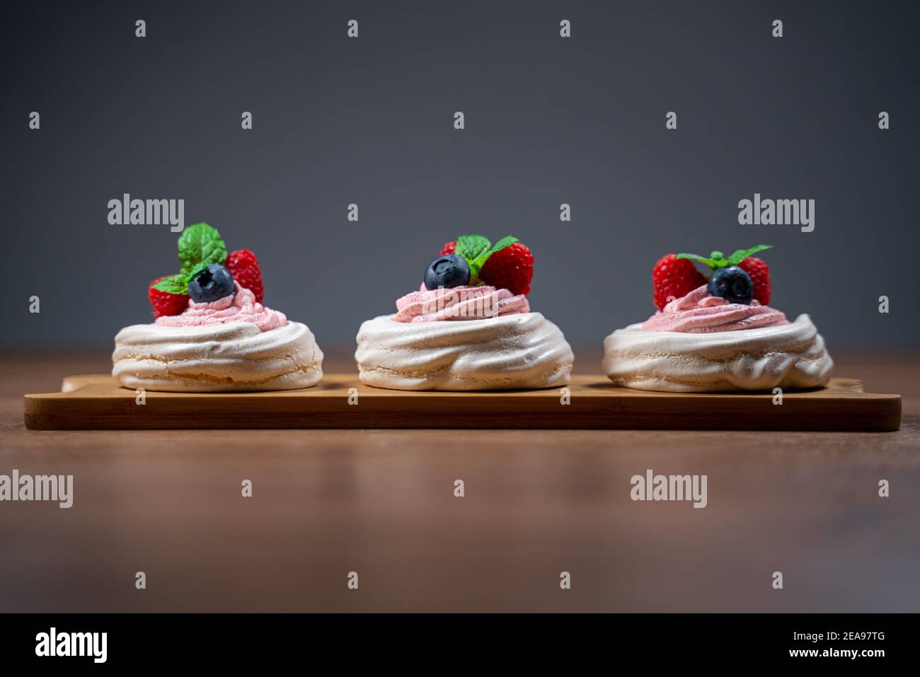 Drei Mini-Pavlova-Kuchen mit Erdbeer-Sahne-Füllung mit frischen Beeren und Minzblättern auf Holzoberfläche dekoriert. Isoliert. Grauer Hintergrund Stockfoto