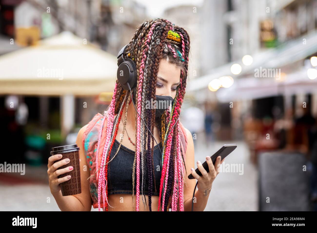 Spielerisch cool Rebell funky Hipster junges Mädchen mit Gesichtsmaske Suchen nach Wiedergabelistenmusik auf dem Mobiltelefon, während Sie auf das Gerät gehen City Street Stockfoto