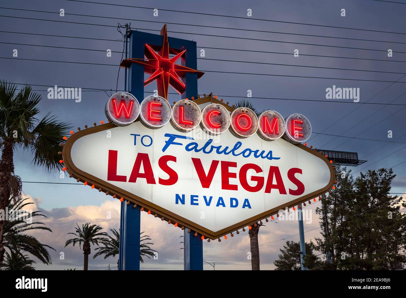 Blick in die Abenddämmerung auf das berühmte Welcome to Fabulous Las Vegas Schild mit Palmen und Dachgitter im Hintergrund. Stockfoto