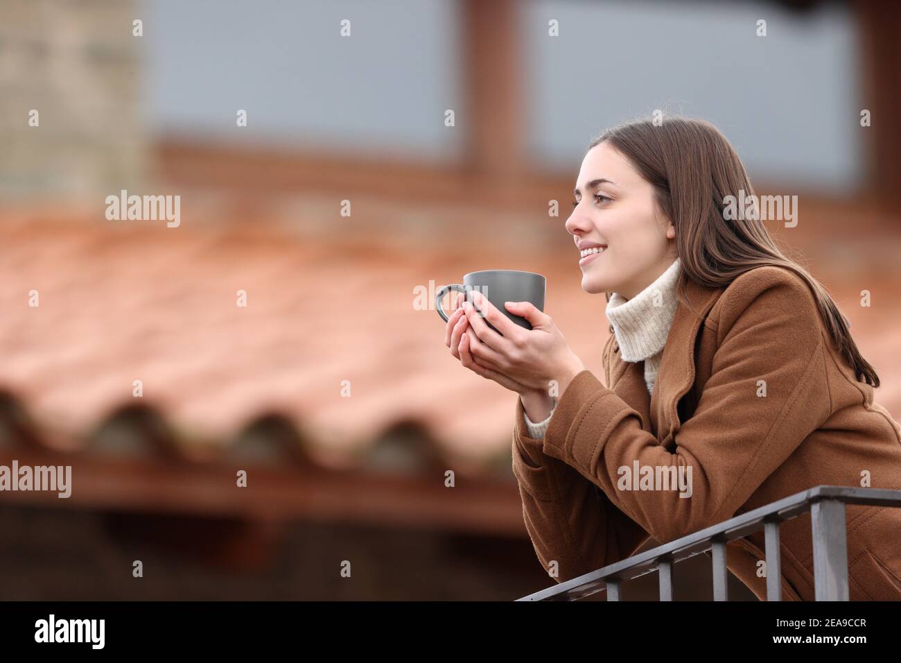 Glückliche Frau, die Aussicht und Kaffee trinken auf einem Balkon Im Winter zu Hause Stockfoto