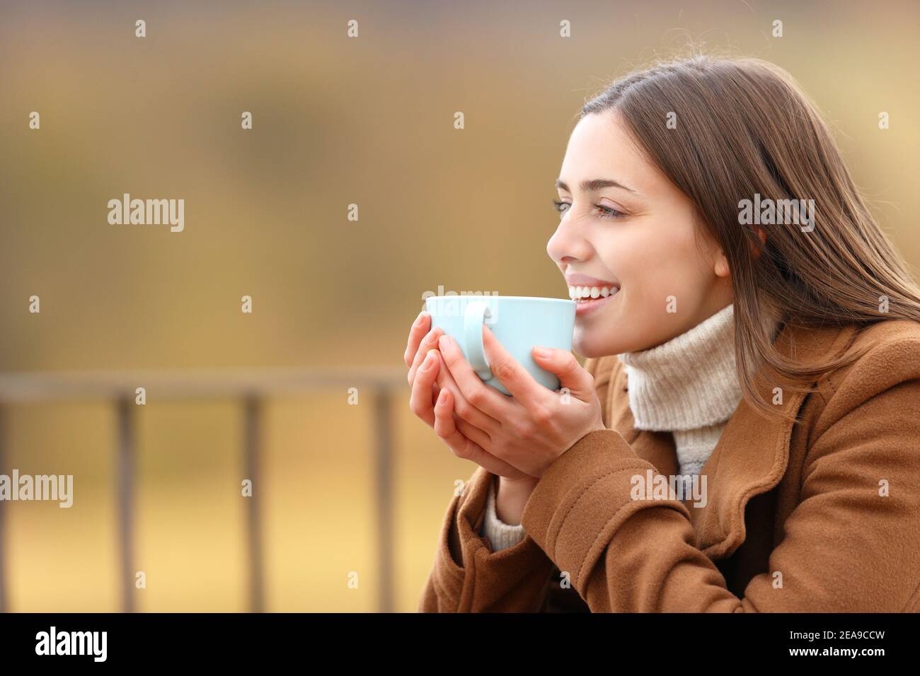 Glückliche Frau, die Kaffee trinkt und die Aussicht auf der Terrasse betrachtet Winter in den Bergen Stockfoto