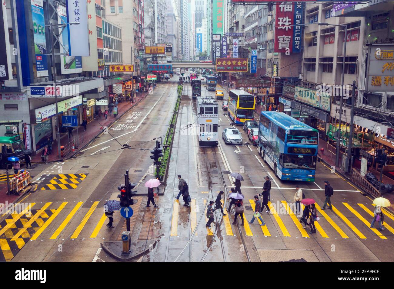 Hongkong, China. Hennessy Road, Causeway Bay. Fußgänger überqueren Straße im Regen. Öffentliche Verkehrsmittel Busse und Straßenbahn. Stockfoto