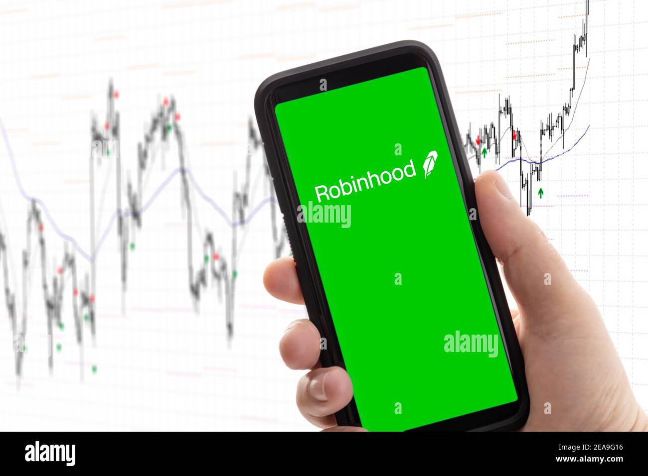Galicia, Spanien; 08. februar 2020: Hand mit Mobiltelefon mit Logo des Maklers Robinhood auf dem Bildschirm und Aktienchart im Hintergrund. App für den Handel, mone Stockfoto