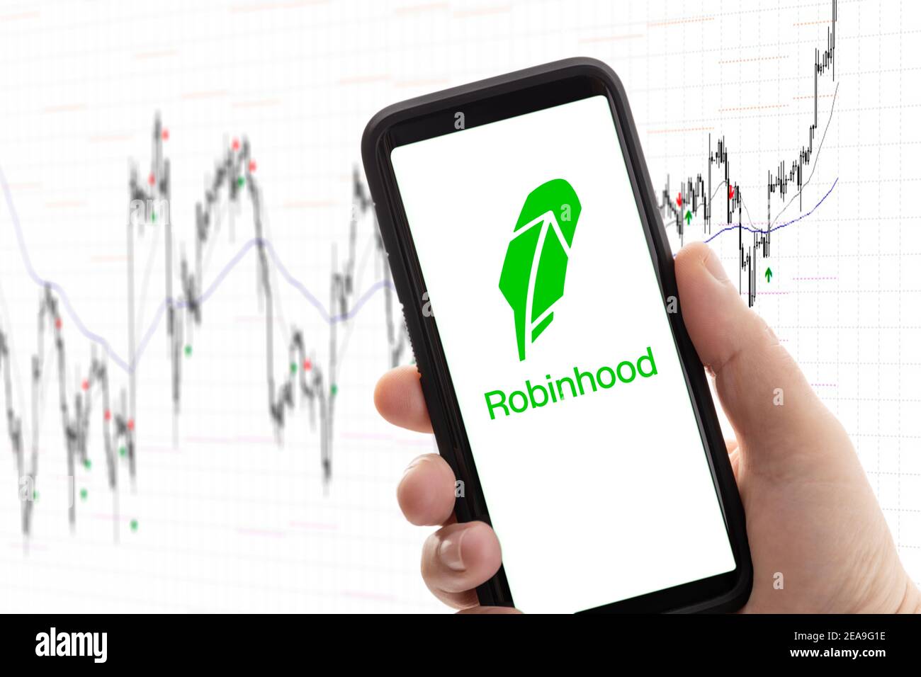 Galicia, Spanien; 08. februar 2020: Hand mit Mobiltelefon mit Logo des Maklers Robinhood auf dem Bildschirm und Aktienchart im Hintergrund. App für den Handel, mone Stockfoto