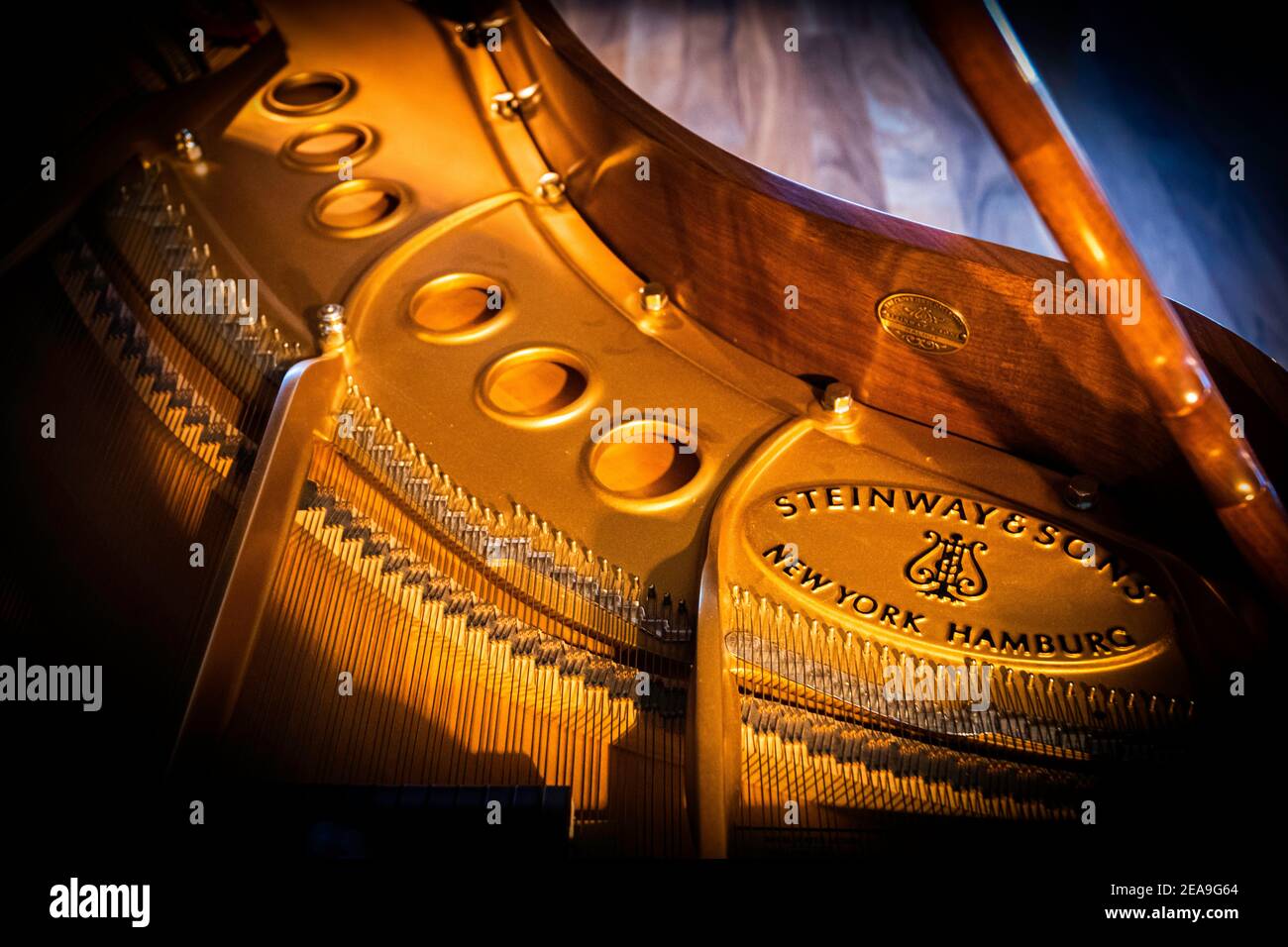 Das Resonanzboden eines Steinway M, der durch ein Fenster über dem Klavier von etwas Sonnenlicht beleuchtet wird. Es ruht auf einem dicken Hartholzboden. Stockfoto