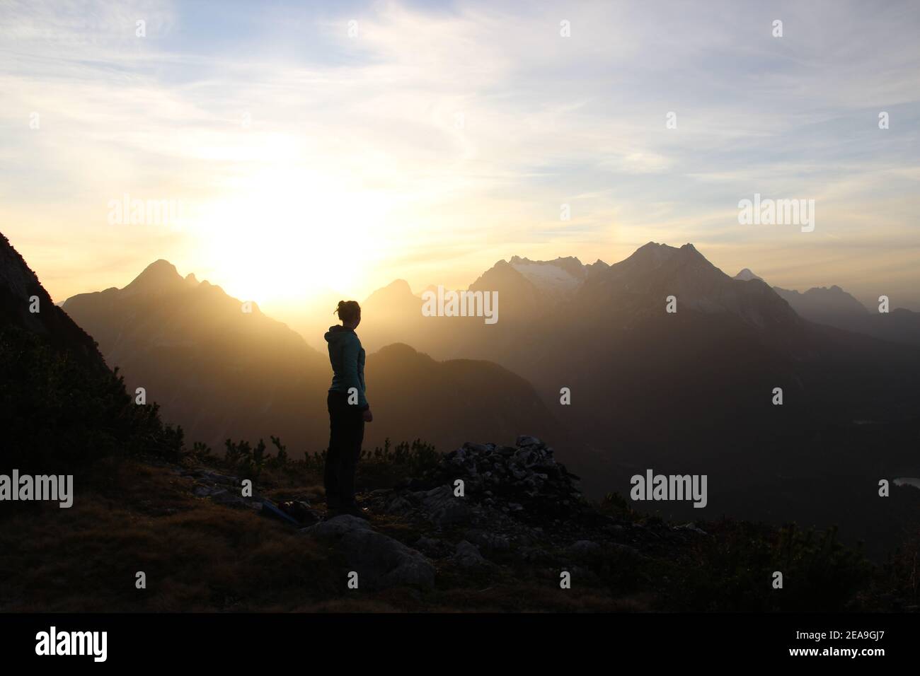 Junge Frau im Sonnenuntergang Richtung Wettersteingebirge, Arnspitze, im Hintergrund die Zugspitze, aufgenommen auf Gamseck oberhalb der Mittenwalder Hütte Stockfoto