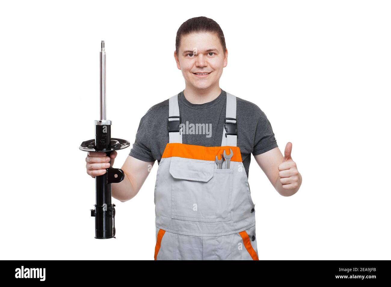 Lächelnder Automechaniker in grauer Uniform mit Schraubenschlüssel Tasche hält in den Händen Auto Ersatzteile der Aufhängung System-Stoßdämpfer vorn und s Stockfoto