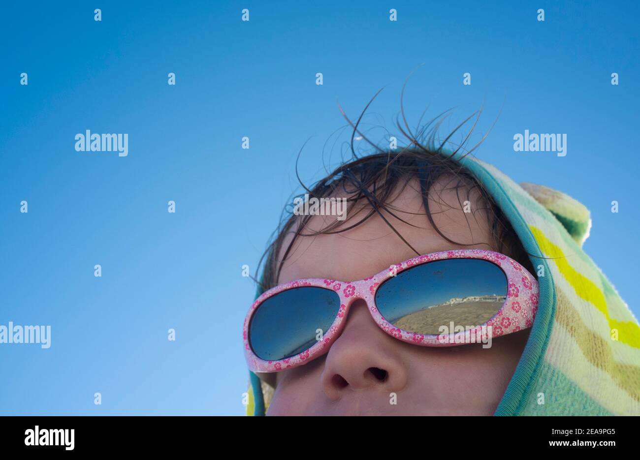 3 Jahre kleiner Junge, der nach dem Schwimmen ein Sonnenbad nimmt. Er trägt Kapuzenponcho Handtuch und Sonnenbrille Stockfoto