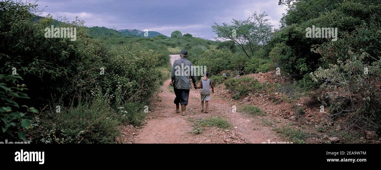 Ein Kind geht mit seinem Vater auf einem unbefestigten Weg. Ein Mann hält die Hand eines Kindes, das auf dem Weg aufwacht. Stockfoto