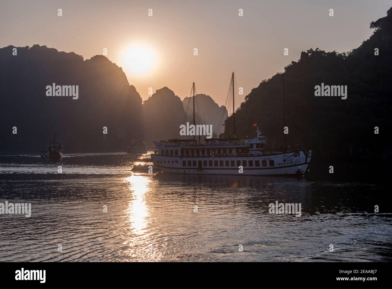 Touristenboot von der aufgehenden Sonne hinterleuchtet, Halong Bay, Vietnam Stockfoto