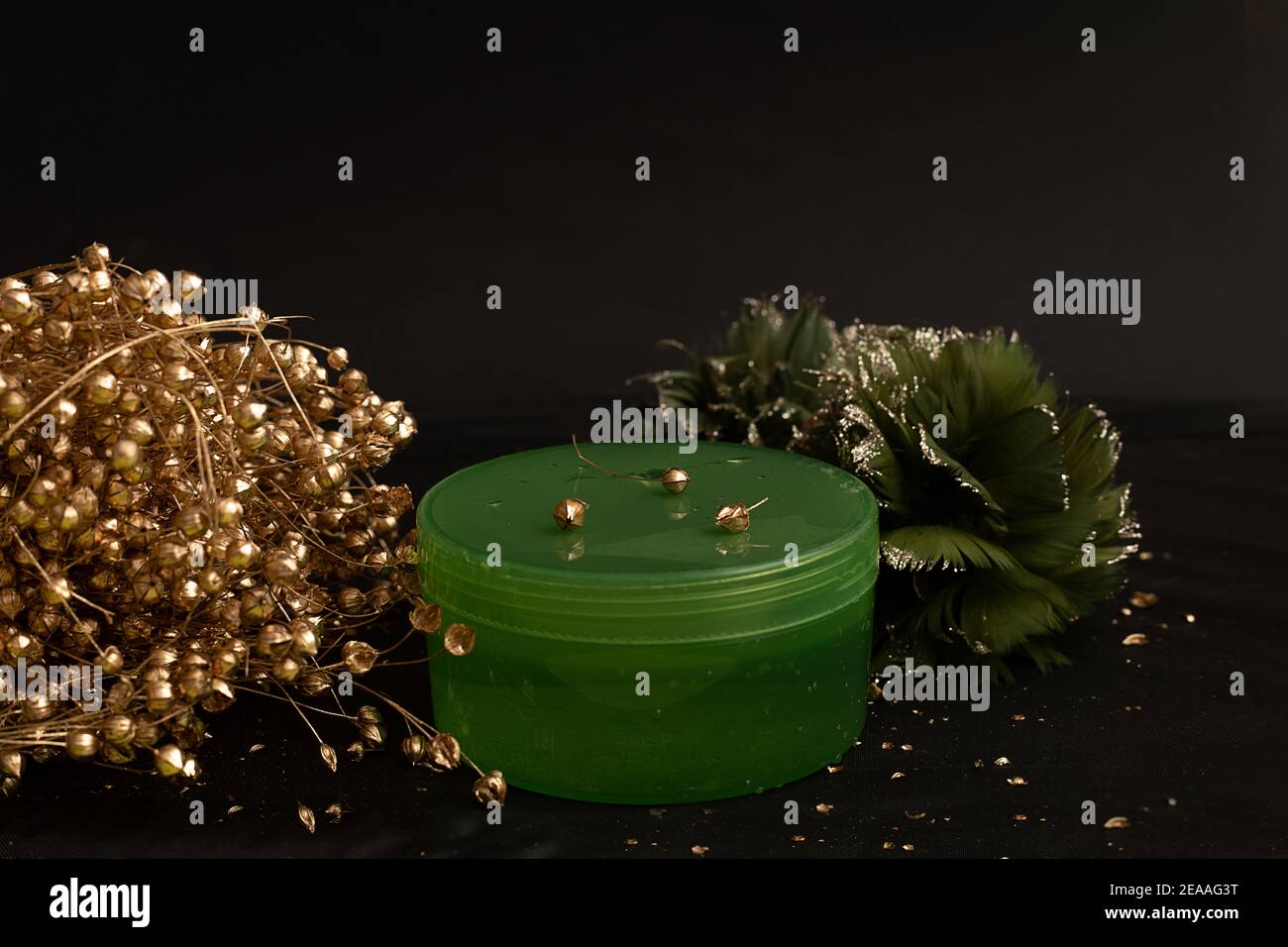 Grüner Plastikbehälter für Balsam-Creme-Kosmetik auf schwarzem Hintergrund mit goldenen Elementen. Hautpflegekonzept, Anti-Aging-Programm. Modell Stockfoto