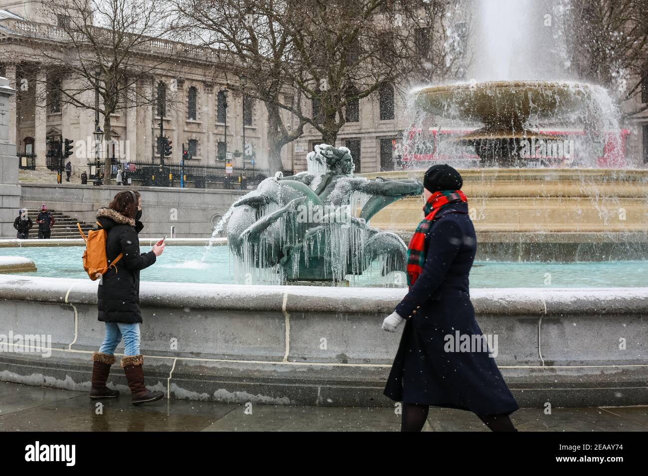 London, Großbritannien. Februar 2021, 08. UK Wetter: Frauen sehen einen eisbedeckten gefrorenen Brunnen auf dem Trafalgar Square. Verursacht durch Sturm Darcy. Quelle: Waldemar Sikora Stockfoto