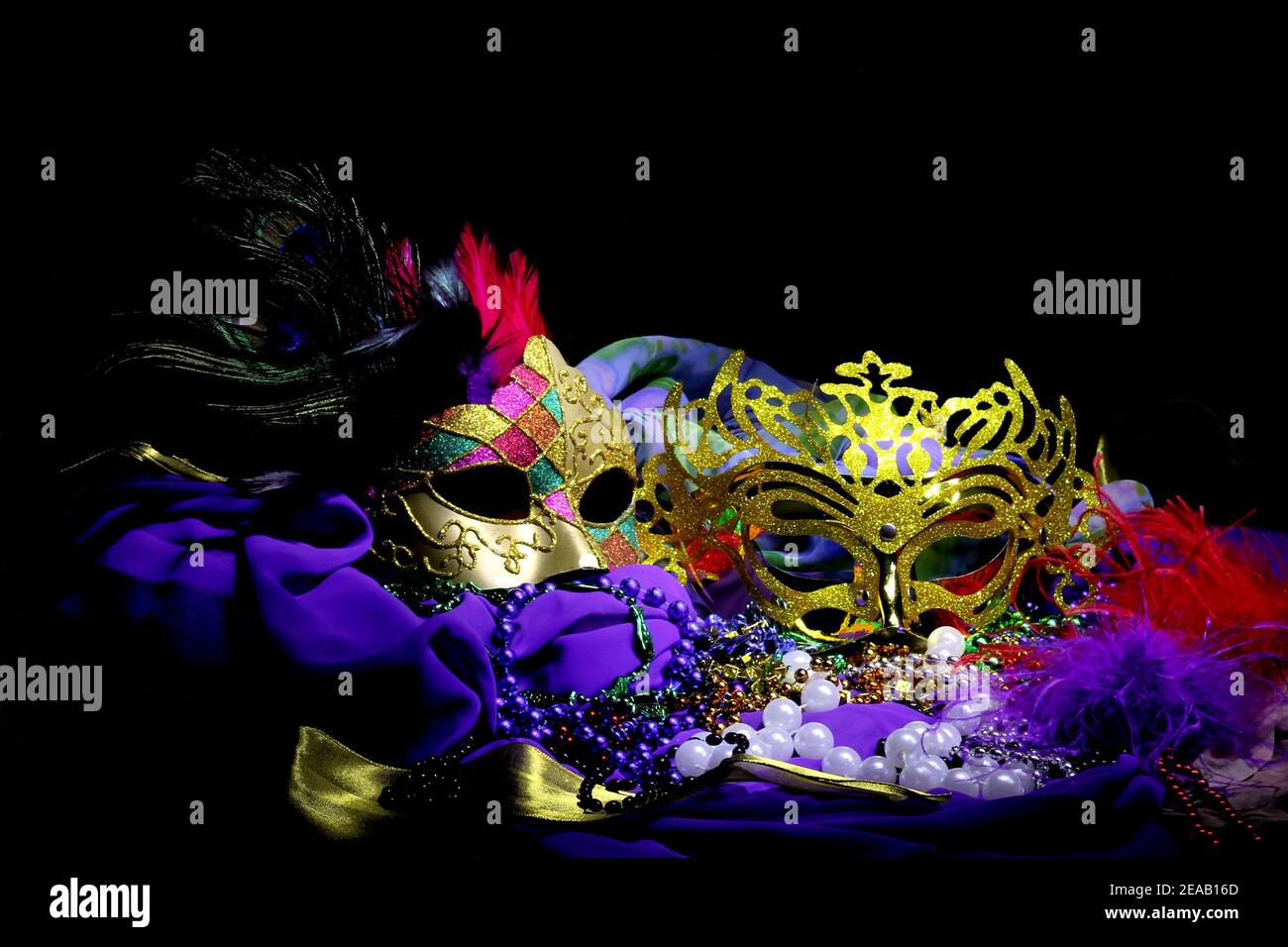 Zwei verzierte Goldmasken mit Federn und Satinstoff sitzen in einem farbenfrohen Stillleben-Arrangement. Stockfoto