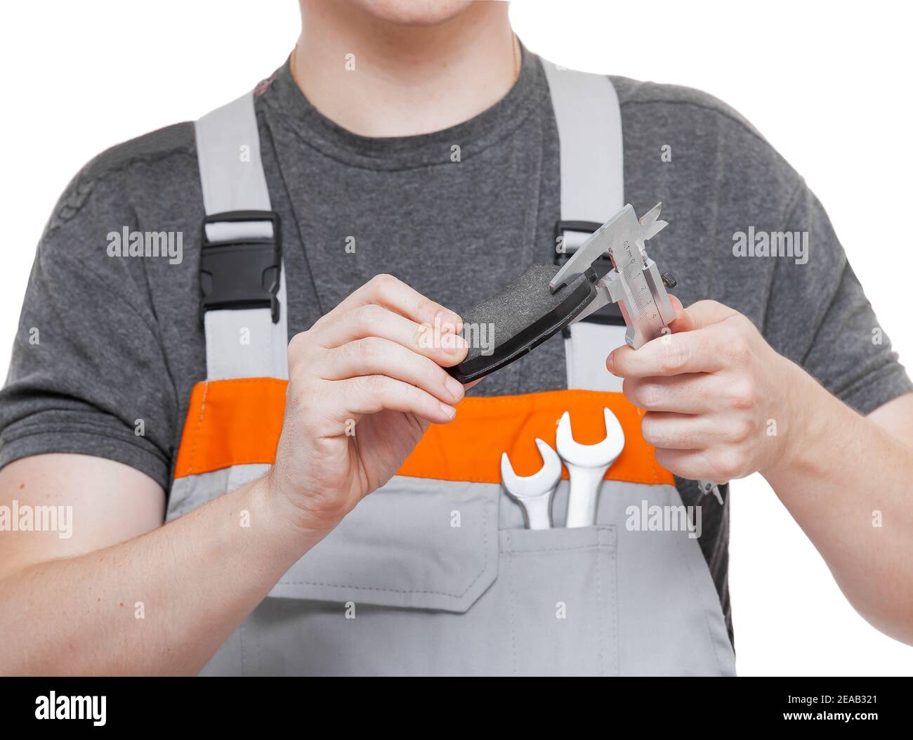 Arbeiter in der Uniform des Mechanikers mit dem Schraubenschlüssel in den Taschenhalten Bremsbeläge und Bremssättel in den Händen messen Asbestgröße von Auto Bremsen Ersatzteil mit eng Stockfoto