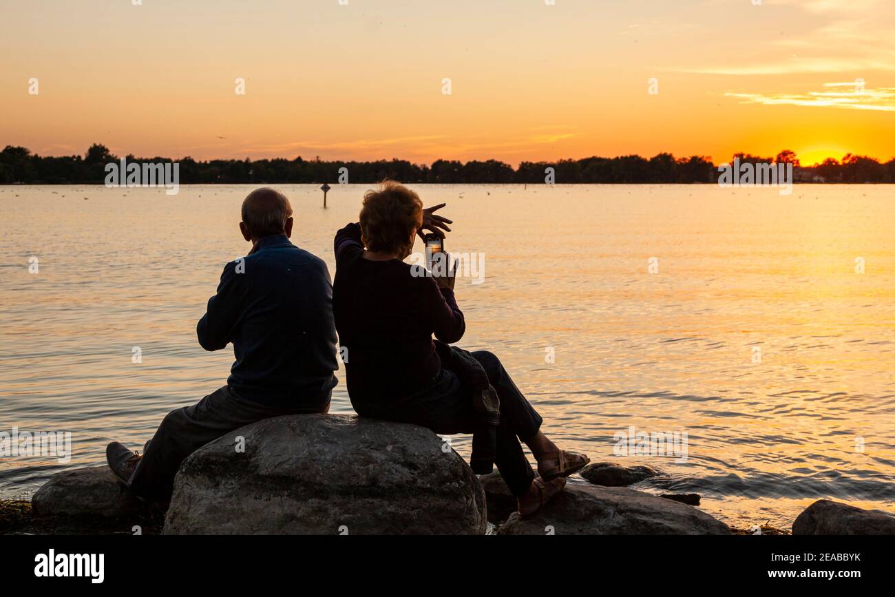 Ein Seniorenpaar in Silhouette, genießen den Sonnenuntergang am See. Stockfoto