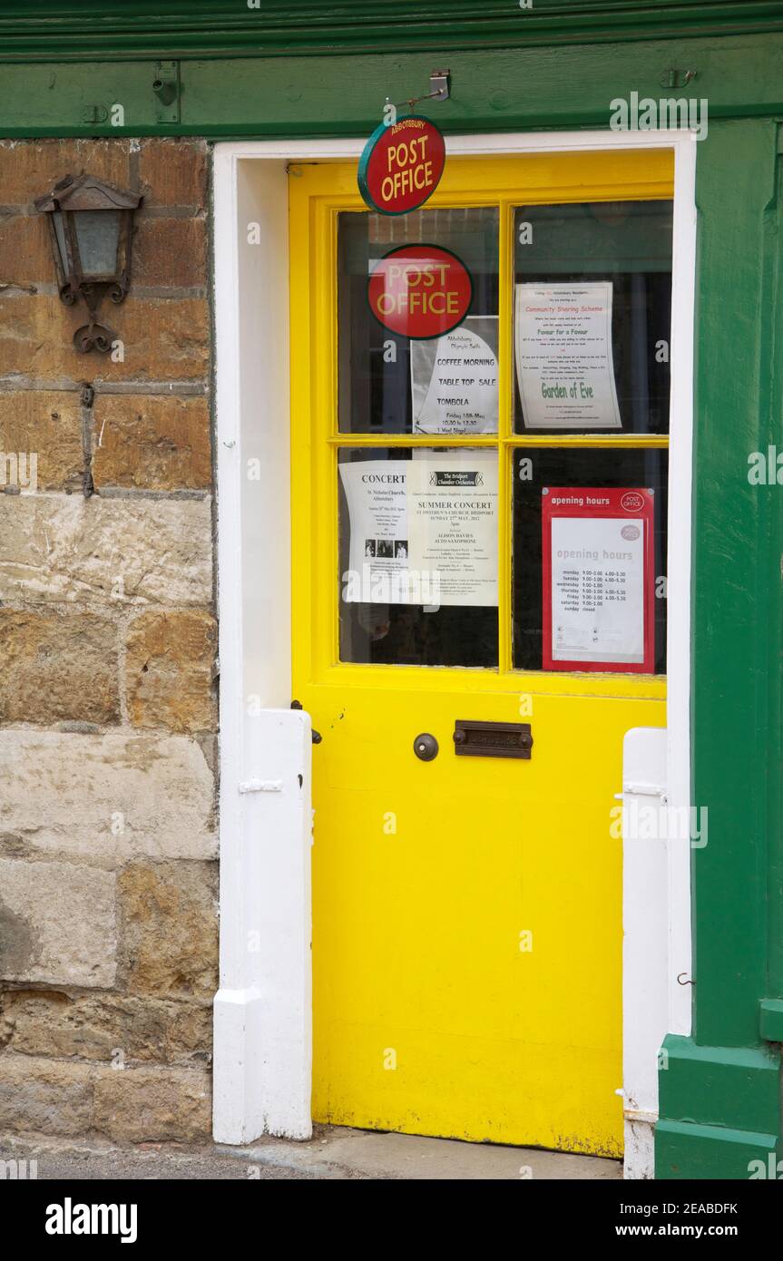 Die leuchtend gelbe Tür des alten Dorfpostamtes in Abbotsbury. Ein wichtiger Knotenpunkt für diese kleine ländliche Gemeinde. Dorset, England, Vereinigtes Königreich. Stockfoto