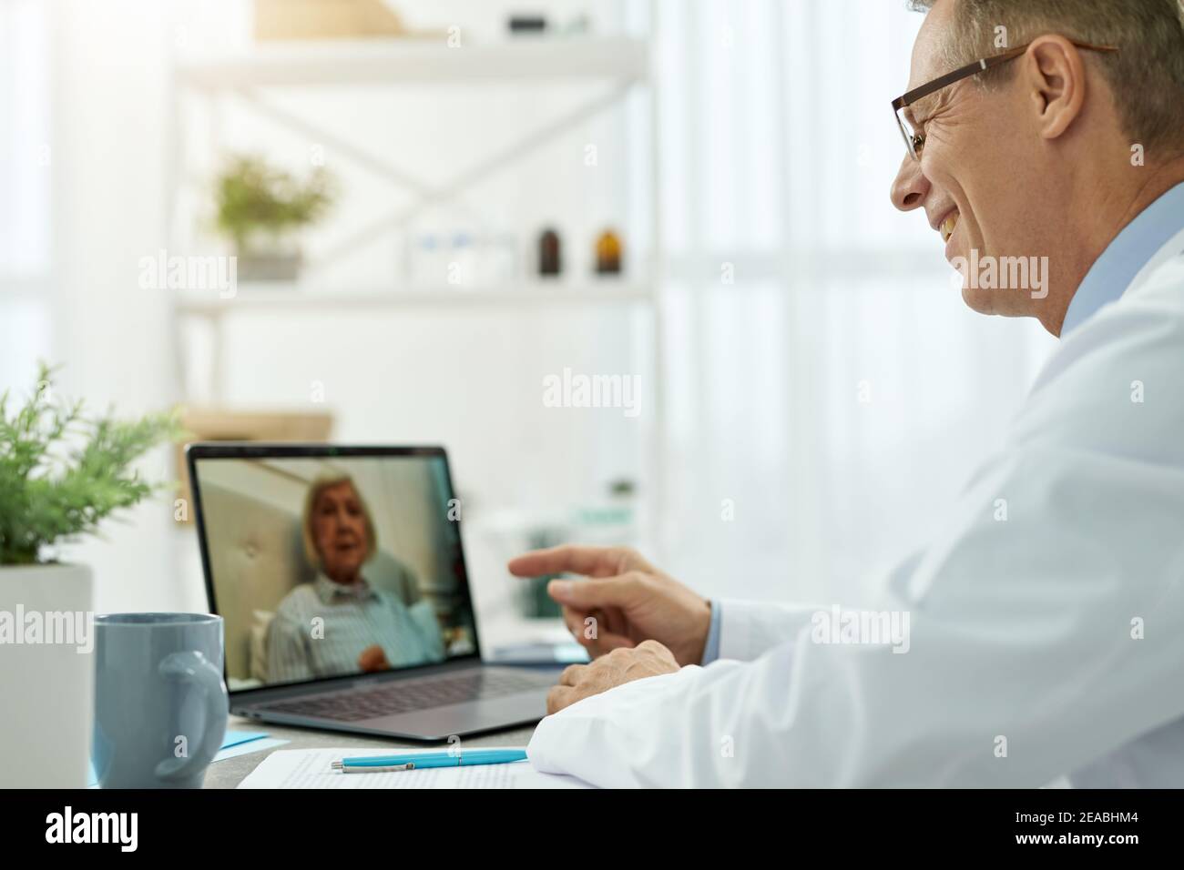 Fröhlicher Arzt, der Online-Beratung für alte Frau in der Klinik Stockfoto