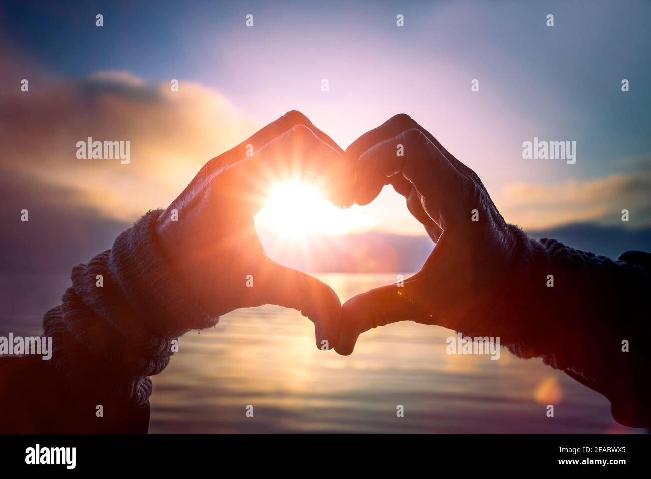 Herz aus Händen mit Sonnenlicht auf dem See Stockfoto