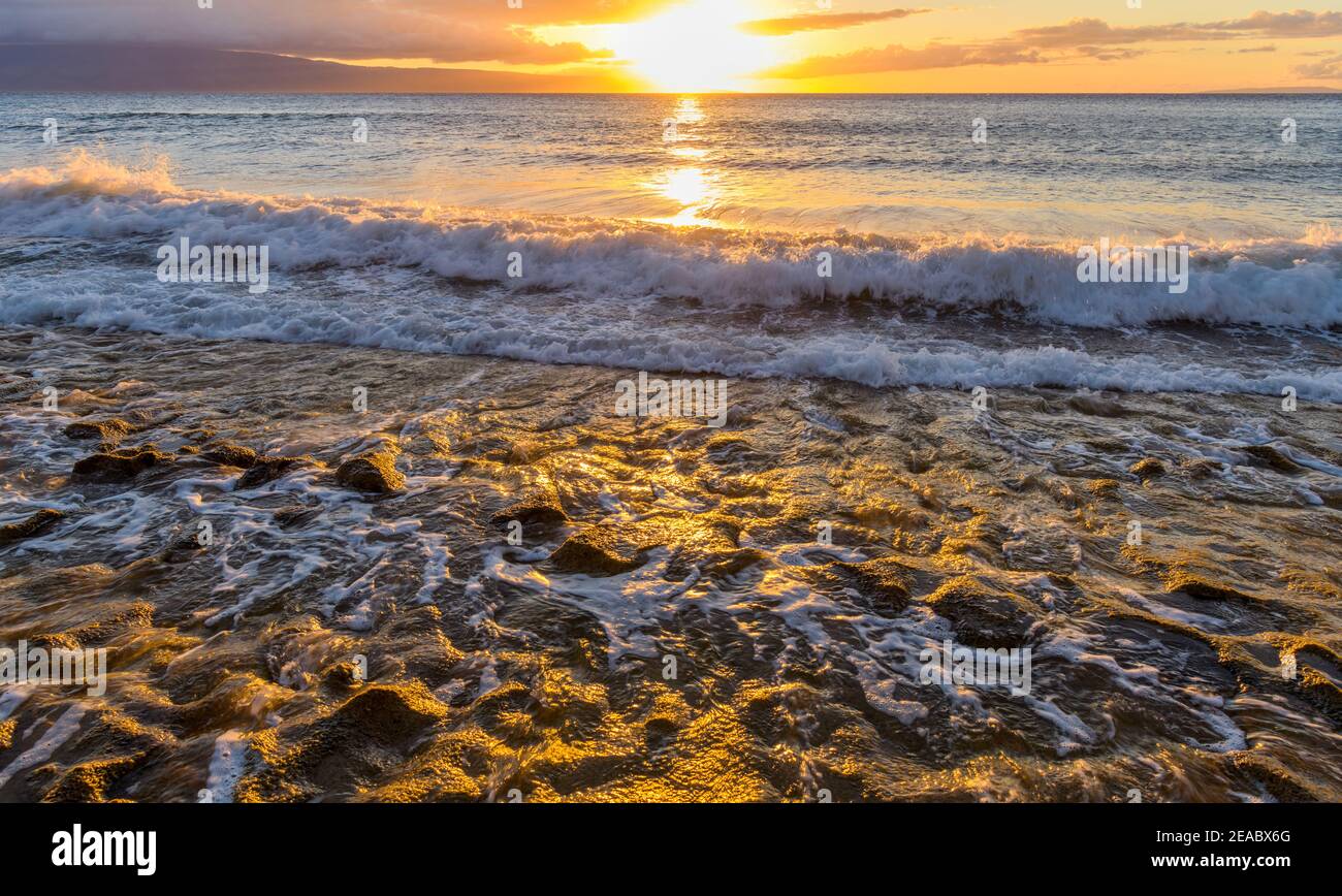 Golden Sunset - heller Sonnenuntergang Blick auf starke Wellen rauschen in und aus der felsigen Küste an der Nordwestküste von Maui Island, Hawaii, USA. Stockfoto