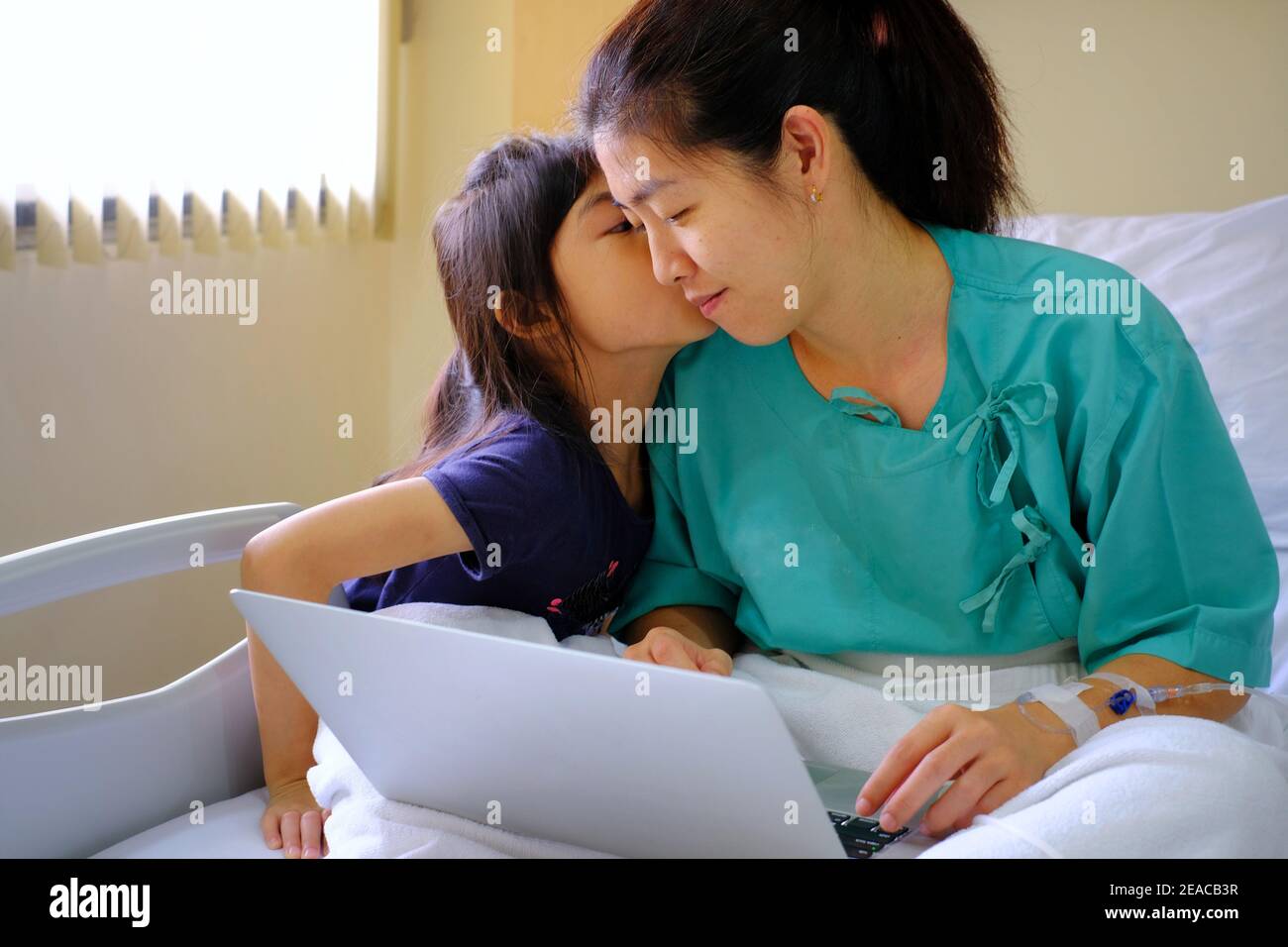Eine Halbkörperaufnahme einer arbeitsreichen Geschäftsfrau, die in einem Krankenhausbett mit intravenöser Injektion in ihrem Arm sitzt und sich von der Operation erholt, während sie einen Laptop benutzt Stockfoto
