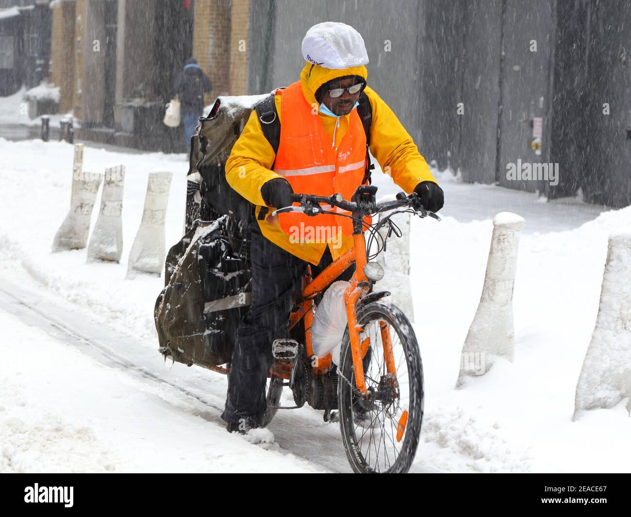 Eine Lieferperson, die einen schlechten Tag hat und versucht, in die Pedale zu treten Ein stark beladenes Fracht-E-Bike mit mechanischen Problemen (leere Batterie/Motor) Während eines Schneesturms in NYC Stockfoto