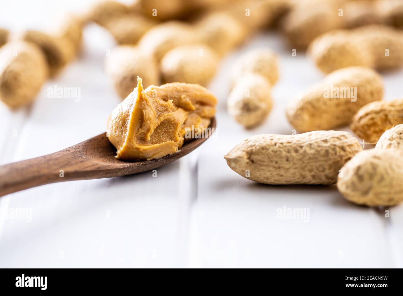Erdnussbutter in Holzlöffel und Erdnüsse auf weißem Tisch. Stockfoto