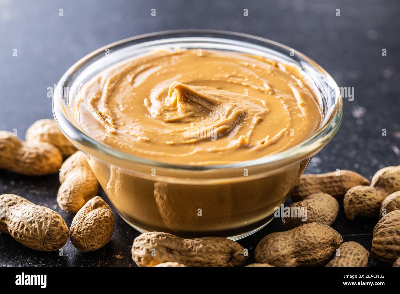 Erdnussbutter in Schale und Erdnüsse auf schwarzem Tisch. Stockfoto