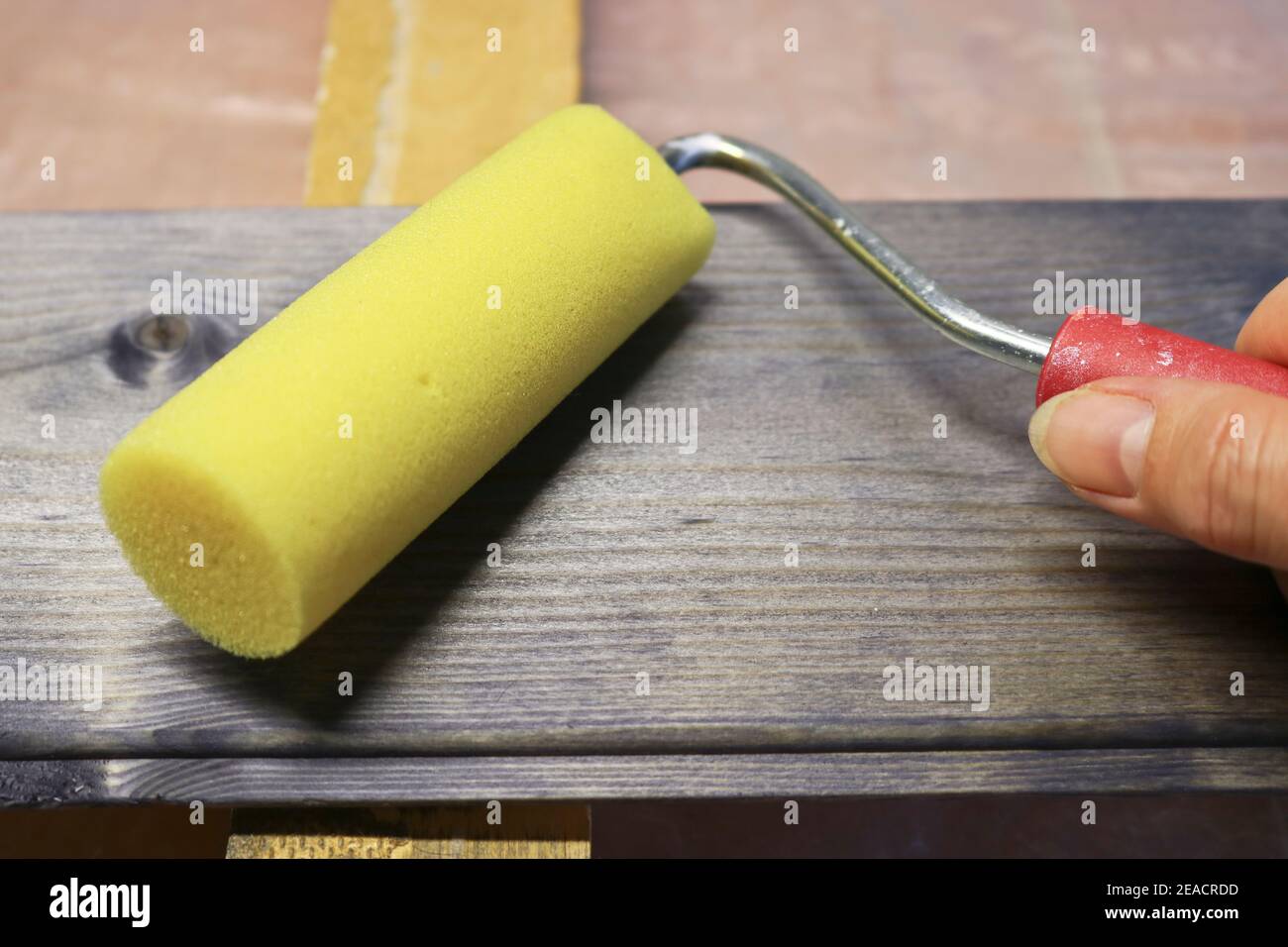 Umgang mit einem Kiefernholzbrett mit einem dunklen Fleck mit einer Schaumwalze. Zimmerei und Malerei arbeitet. Stockfoto