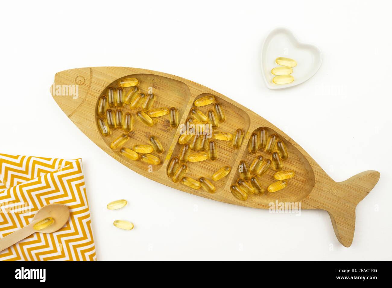 Gelbe Kapseln von Omega 3 liegen auf einem Holzteller In Form des Fisches Stockfoto