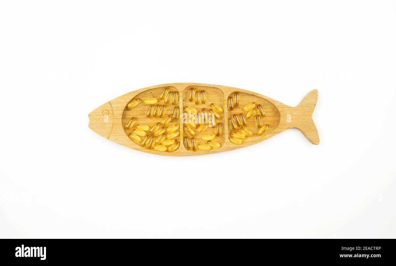 Gelbe Kapseln von Omega 3 liegen auf einem Holzteller In Form des Fisches Stockfoto