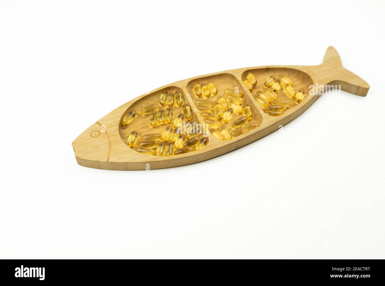 Gelbe Kapseln von Omega 3 liegen auf einem Holzteller In Form des Fisches Stockfoto