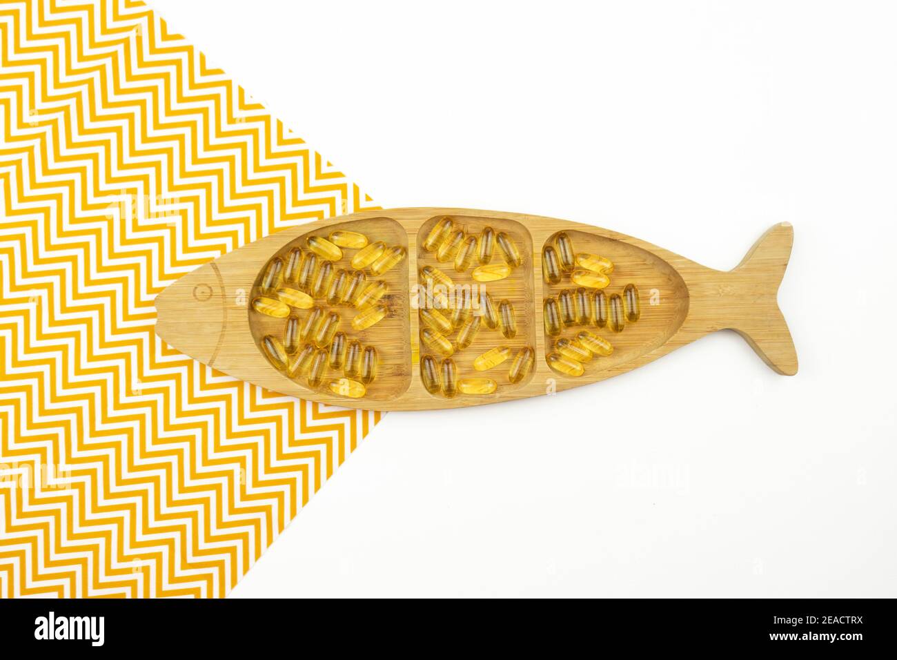 Gelbe Kapseln von Omega 3 liegen auf einem Holzteller In Form des Fisches Stockfoto