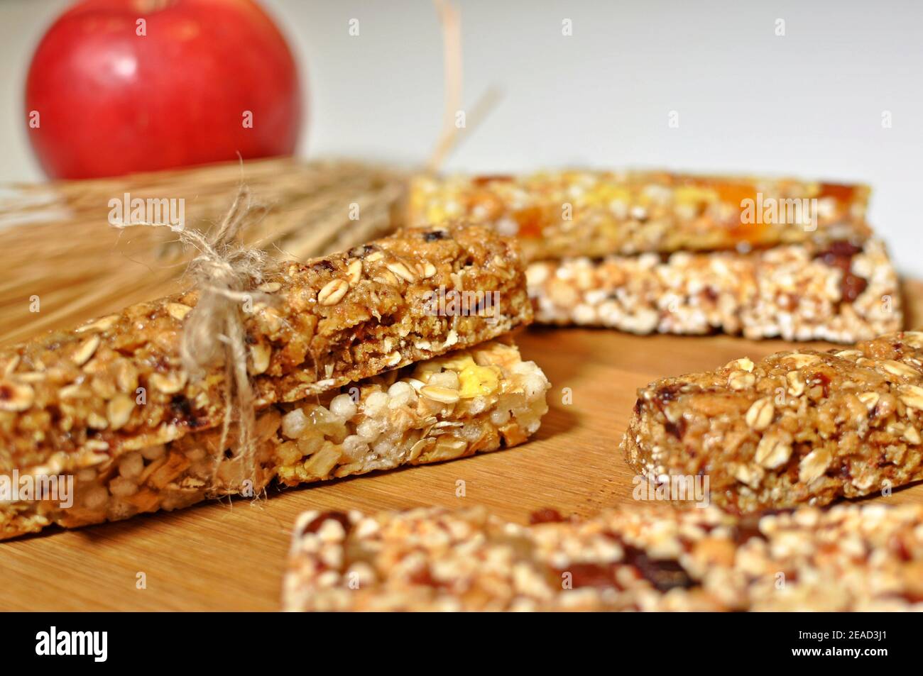 Seitenansicht Nahaufnahme von süßen Scheiben gesunden Getreides Riegel mit getrocknetem Weizen und Früchten auf braunem Holztisch Und roten Apfel Hintergrund Stockfoto