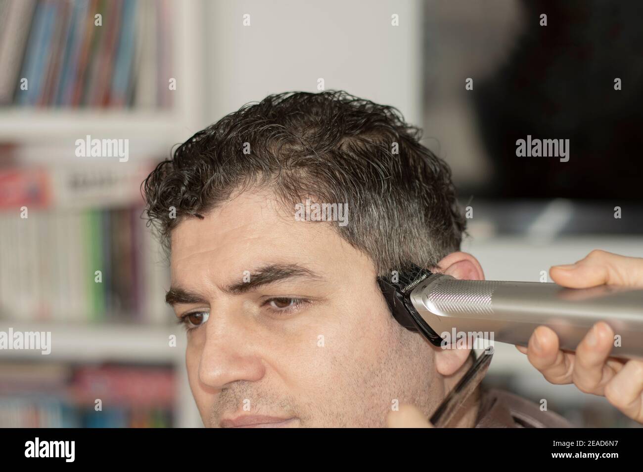 Junge Frau schneidet ihrem Mann die Haare zu Hause während der Pandemie, zu Hause bleiben Stockfoto