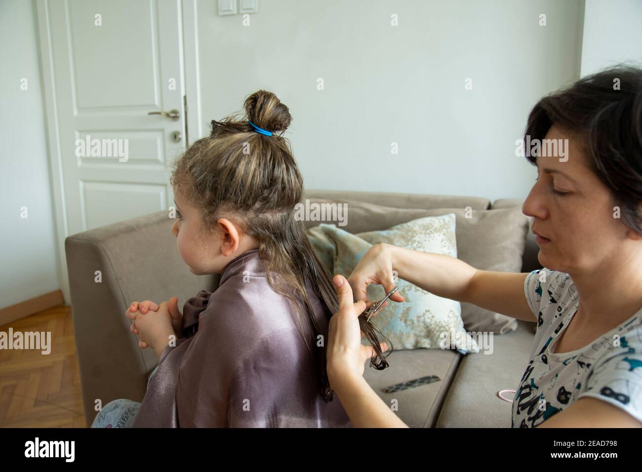 Junge Frau schneidet ihre Tochter die Haare zu Hause während der Pandemie. Bleiben Sie zu Hause. Stockfoto