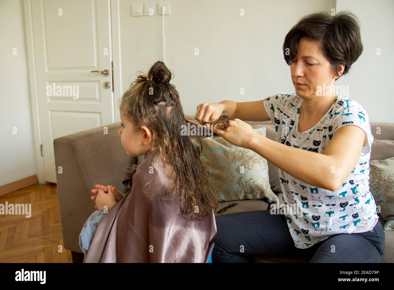 Junge Frau schneidet ihre Tochter die Haare zu Hause während der Pandemie. Bleiben Sie zu Hause. Stockfoto