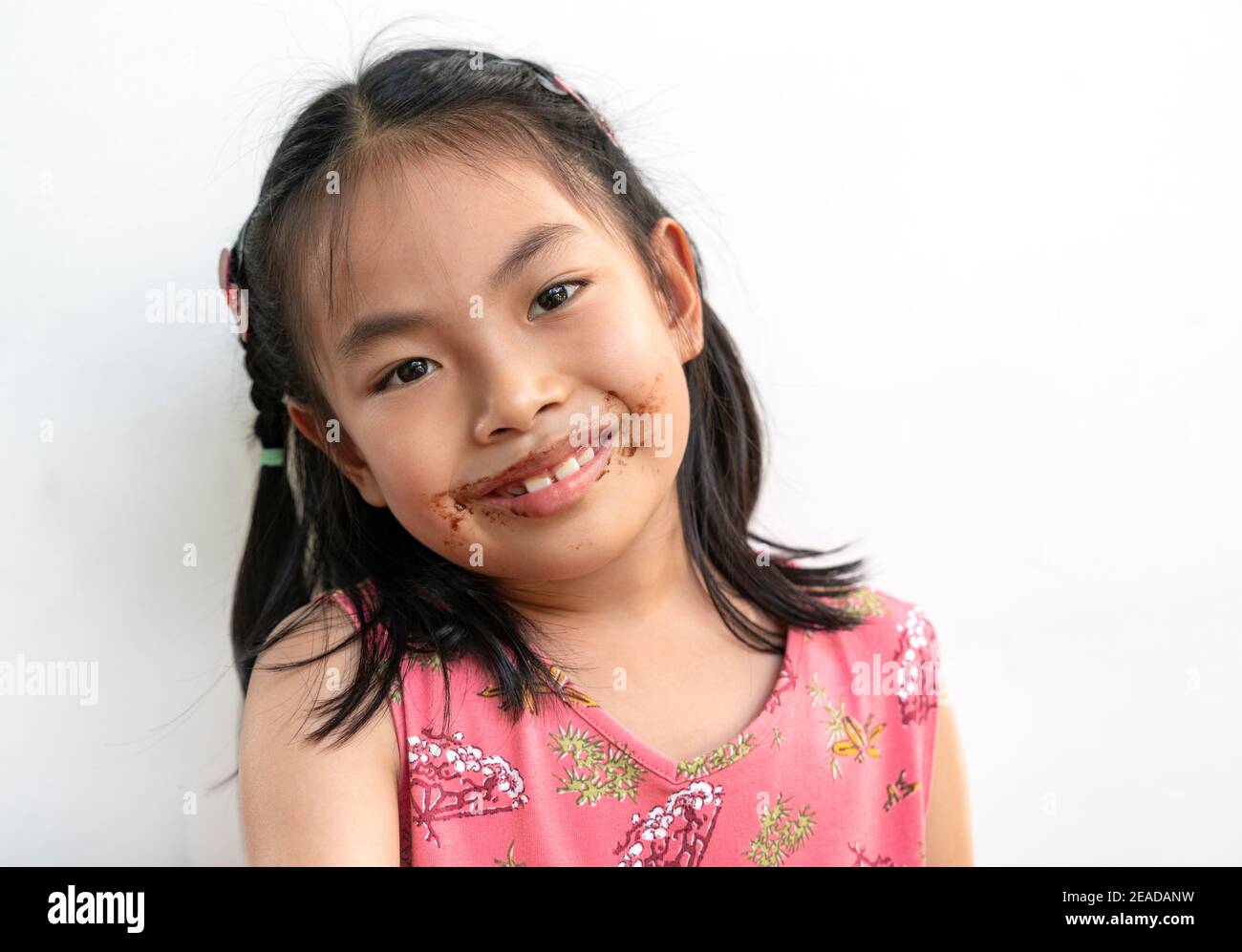 Portrait schönes Kind Mädchen mit Schokolade um den Mund, großes Lächeln auf niedlichen Gesicht, schwarze Haare, trägt schöne rosa Kleid. Schönes asiatisches Kind Stockfoto